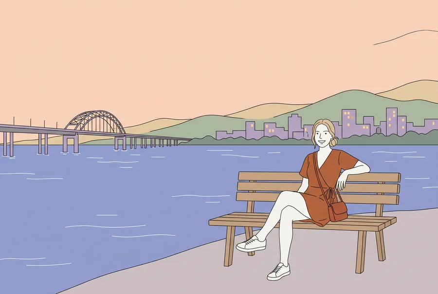 La jeune femme dessinée du guide assise sur un banc au bord du fleuve, au crépuscule; en face, une ville et un long pont avec une arche